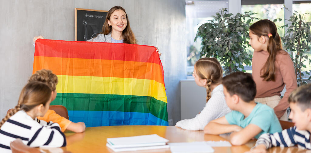 Eine Lehrerin zeigt ihrer Klasse eine Regenbogenflagge und erklärt LGTBQAI+