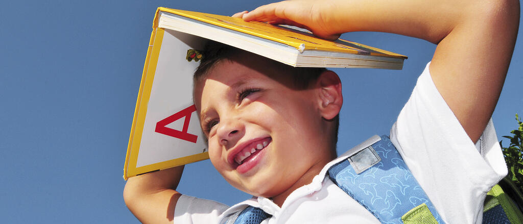 Junge hält ein Schulbuch über seinen Kopf