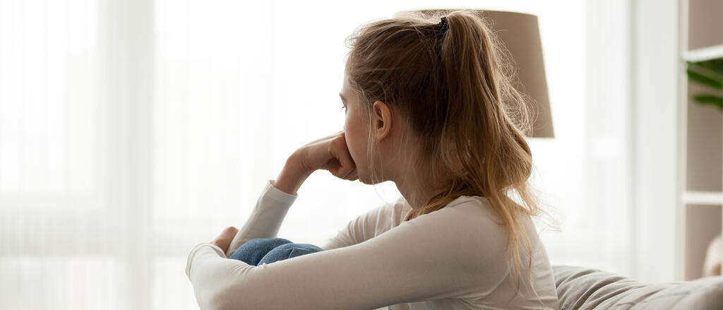 Ein Mädchen kauert traurig auf ihrem Bett, den Kopf auf die Hände gestützt