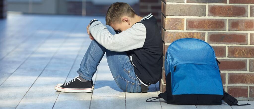 Ein Junge sitzt traurig im Schulhof, den Kopf auf die Knie gesenkt