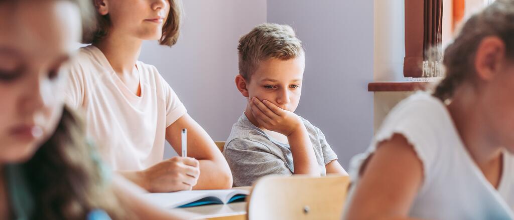 Ein Junge sitzt mit traurigem Gesichtsausdruck im Klassenzimmer